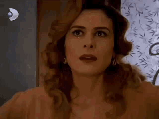a close up of a woman 's face with her eyes closed in front of a curtain with leaves on it