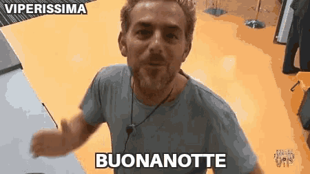 a man with a beard is standing in a room with a yellow floor and says buonanotte .
