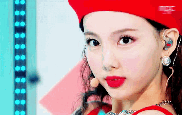 a close up of a woman 's face wearing a red hat and earrings