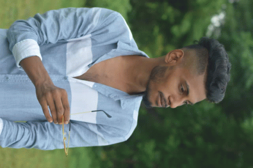 a man in a blue shirt holds a pair of glasses in his right hand