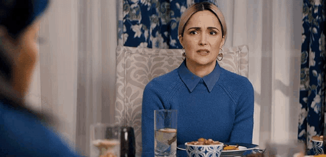 a woman in a blue sweater sits at a table with a plate of food