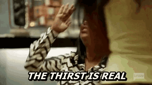 a woman is sitting at a table with her hands up and the words `` the thirst is real '' .