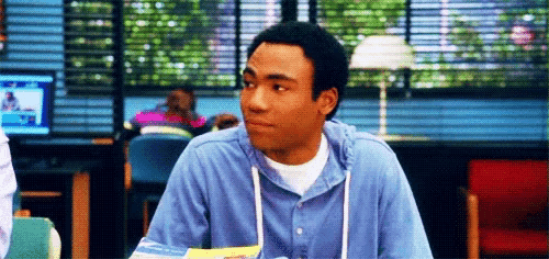 a man in a blue shirt is sitting at a table in a library .