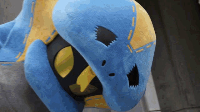 a blue and yellow stuffed animal with a black mouth