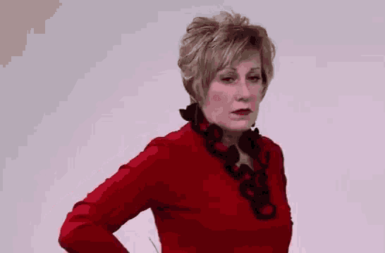 a woman in a red sweater and black necklace is standing with her hands on her hips .
