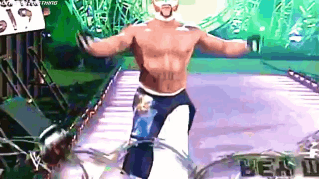 a shirtless wrestling wrestler is walking down a ramp with his arms outstretched .