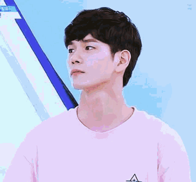 a young man wearing a pink t-shirt is standing in front of a blue wall .