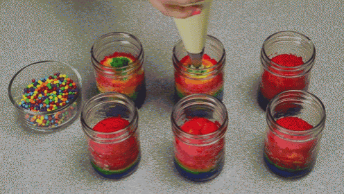 a person is piping frosting into a jar with rainbow colored frosting and sprinkles