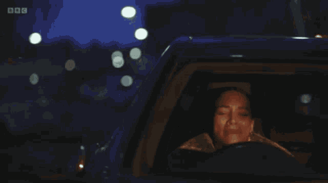 a woman is driving a car at night with her eyes closed and the bbc logo in the background