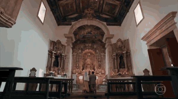 a man in a suit stands in front of an altar in a church with a globe in the corner