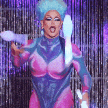 a drag queen in a pink and blue outfit is holding a light