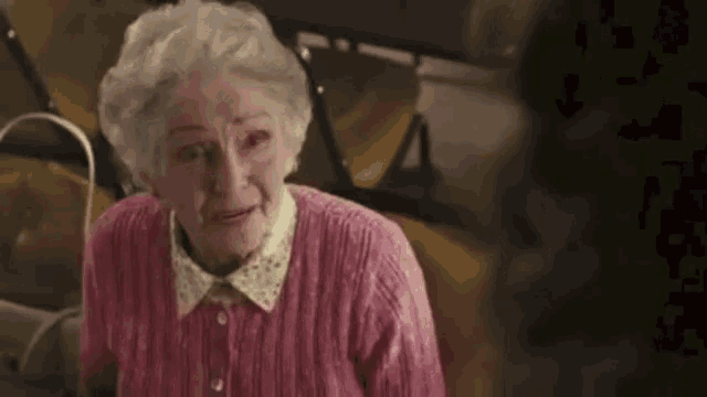 an elderly woman wearing a pink sweater is sitting in a chair .