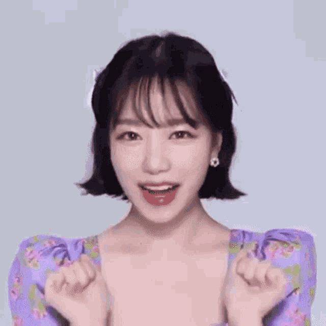 a close up of a woman in a purple dress making a heart with her hands .