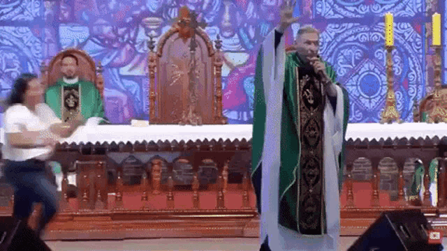 a priest is giving a sermon in front of a stained glass window while a woman watches .