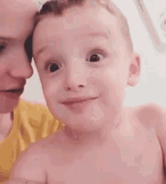 a little boy is smiling and looking at the camera while a woman looks on .