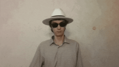 a man wearing a white hat and sunglasses waves his hand