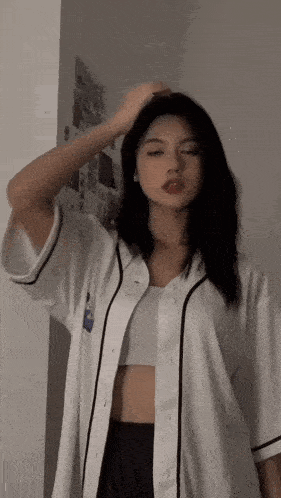 a woman wearing a white baseball shirt and black shorts is standing in front of a wall .