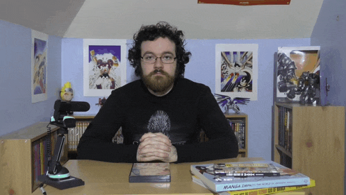a man sits at a desk with a stack of books including one called manga zero