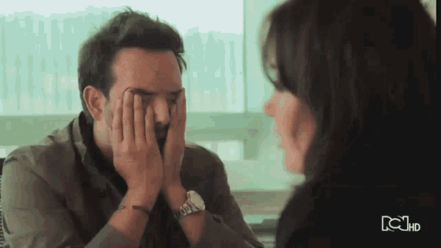 a man covering his face with his hands while a woman looks on with the letters rcj hd visible in the corner