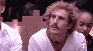 a man with curly hair and a mustache is sitting next to a woman in a room .