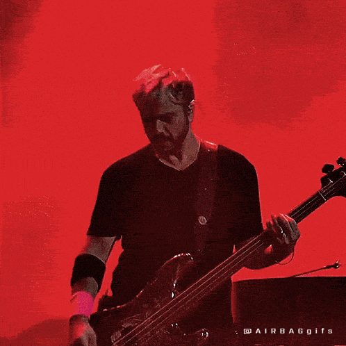 a man in a black shirt is playing a bass guitar on a red background