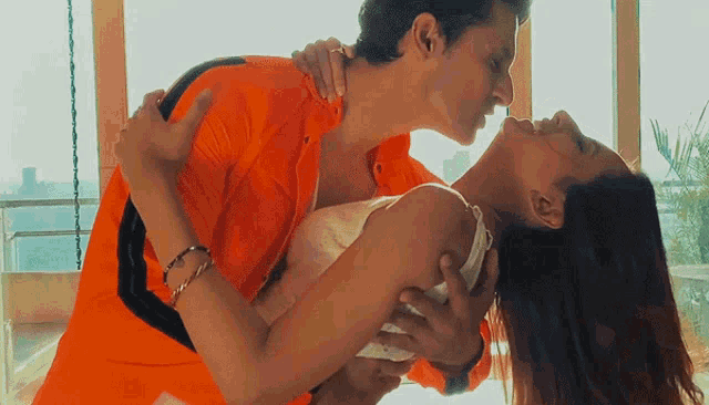 a man in an orange shirt is kissing a woman in a white dress