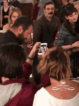 a woman is taking a picture of a man with a cell phone with the name melissa on the back of her shirt
