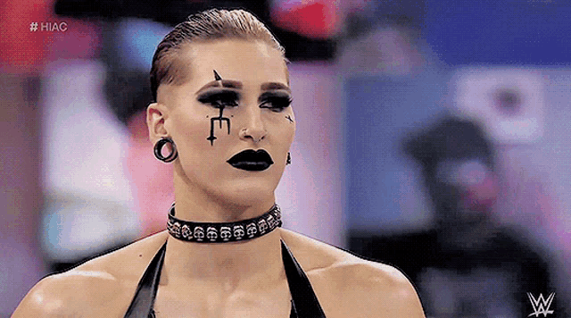 a woman wearing a choker and black makeup has a cross on her face .
