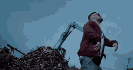 a man in a red jacket is standing next to a pile of scrap metal .