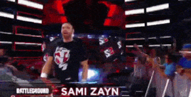 a wrestler named sami zayn is standing in front of a crowd of people .