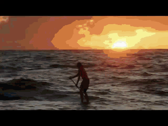 a man stands on a paddle board in the ocean as the sun sets behind him