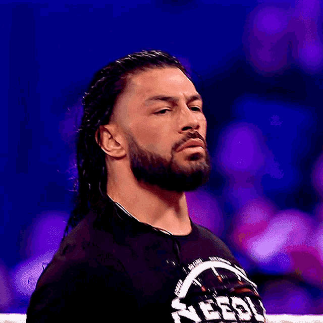 a wrestler with a beard and long hair looks at the camera