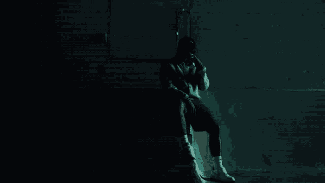 a man in a black hat sits on a staircase in a dark room