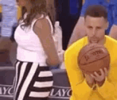 a man in a yellow shirt is holding a basketball while a woman in a white dress stands behind him .