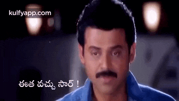 a man with a mustache is wearing a blue shirt and looking at the camera with a caption in a foreign language .