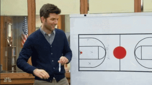 a man in a blue cardigan is standing in front of a white board with a basketball court drawn on it
