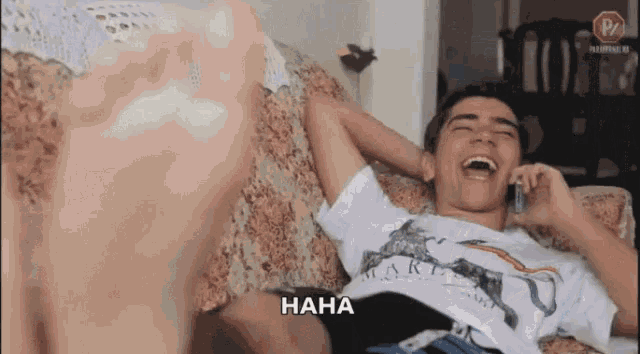 a man is laying on a couch laughing while talking on a cell phone and the word haha is above him