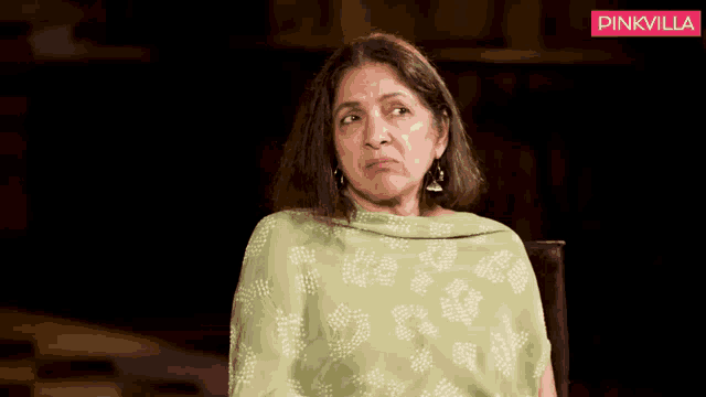 a woman in a green dress is sitting in a chair and looking at the camera .