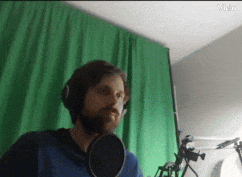 a man with a beard is singing into a microphone with a green screen behind him