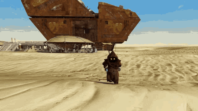a man in a hood is walking in the sand near a large building