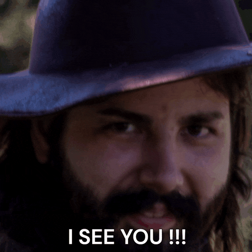 a man with a beard wearing a hat says " i see you !!! "
