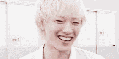a man with blonde hair is laughing with his mouth open in front of lockers .