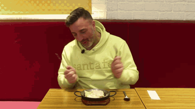 a man wearing a yellow santafe sweatshirt is eating food