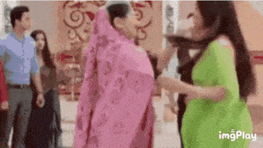 a group of women are dancing in a room with a man in a blue shirt standing behind them .