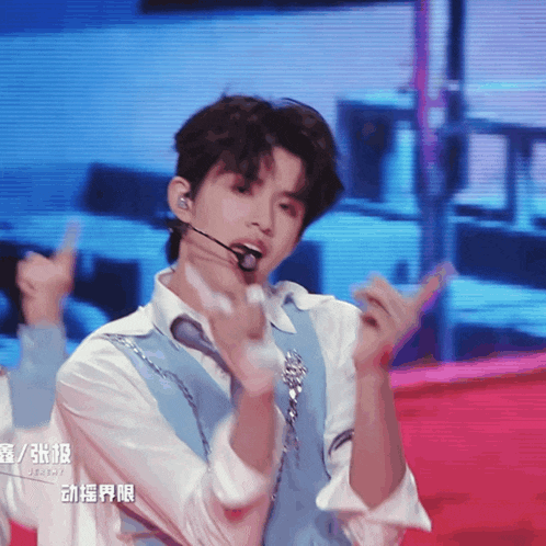a young man wearing a white shirt and a blue vest is giving a thumbs up sign