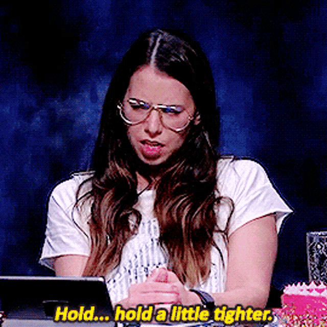 a woman wearing glasses is sitting at a table with a tablet and says hold hold a little tighter