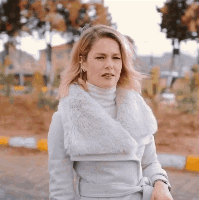 a woman wearing a white coat with a fur collar looks at the camera
