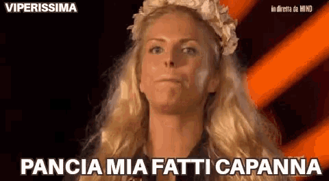 a woman with a flower crown on her head is making a funny face and says pancia mia fatti capanna .