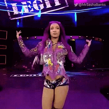 a woman with purple hair is standing on a stage with her arms outstretched in front of a sign .