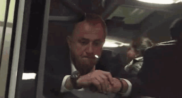 a man in a suit is sitting on a bus smoking a cigarette .